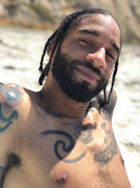 a man with tattoos on his chest laying on the beach